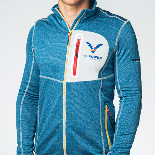 Person trägt eine blaue Reißverschlussjacke mit „AirPower“-Logo auf der Brust und roten Reißverschlussdetails. Das Gesicht ist nicht sichtbar.