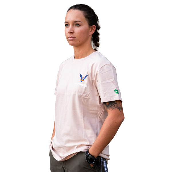 Person in einem beigen T-Shirt mit Logo, die mit ernstem Gesichtsausdruck vor einem weißen Hintergrund steht.