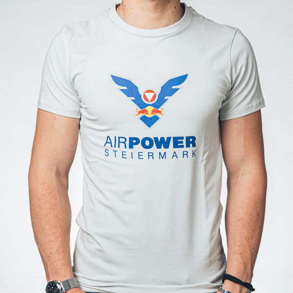 Person, die ein weißes „Air Power Steiermark“-T-Shirt mit einem blau-roten Grafikdesign trägt.