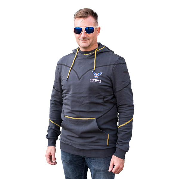 Ein Mann mit Sonnenbrille und dunkelgrauem Kapuzenpullover mit Logo posiert mit den Händen in den Taschen vor einem weißen Hintergrund.