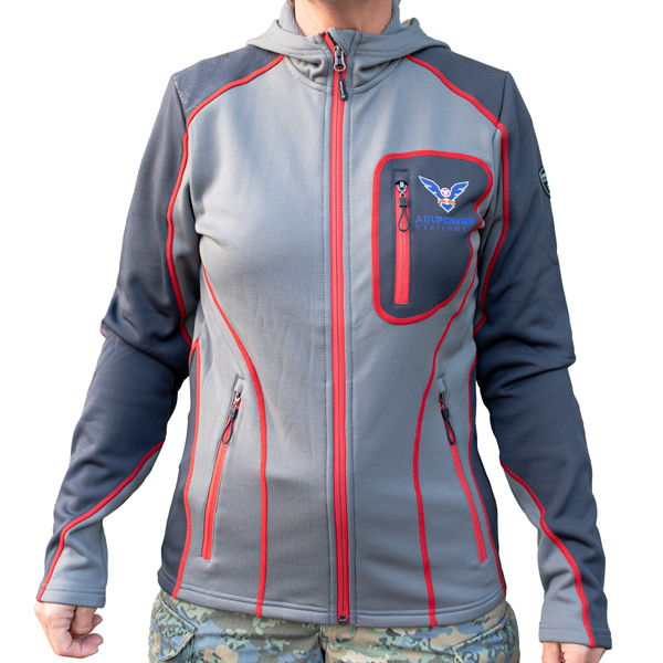 Person trägt eine grau-blaue Jacke mit roten Akzenten und einem Militärabzeichen. Die Jacke hat Vordertaschen und ein Logo.